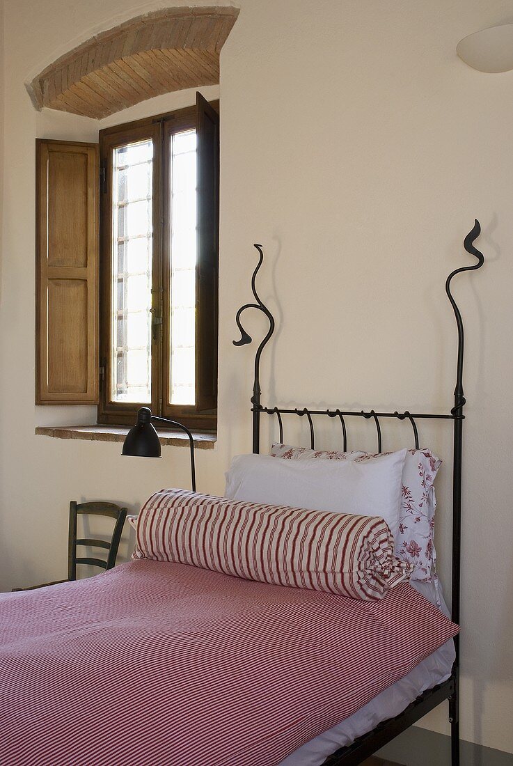 Iron bedstead with pink bed linen and bolster next to a window