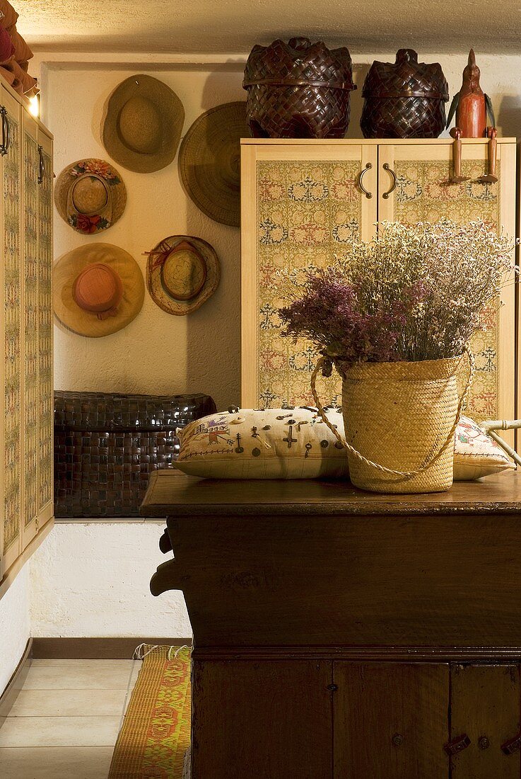 Basket with dried flowers and pillows on a rustic chest of drawers and collection of hats on a wall