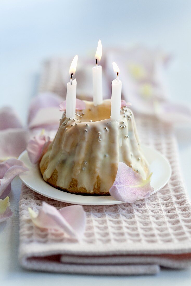 A mini Bundt cake with rose petal icing and candles