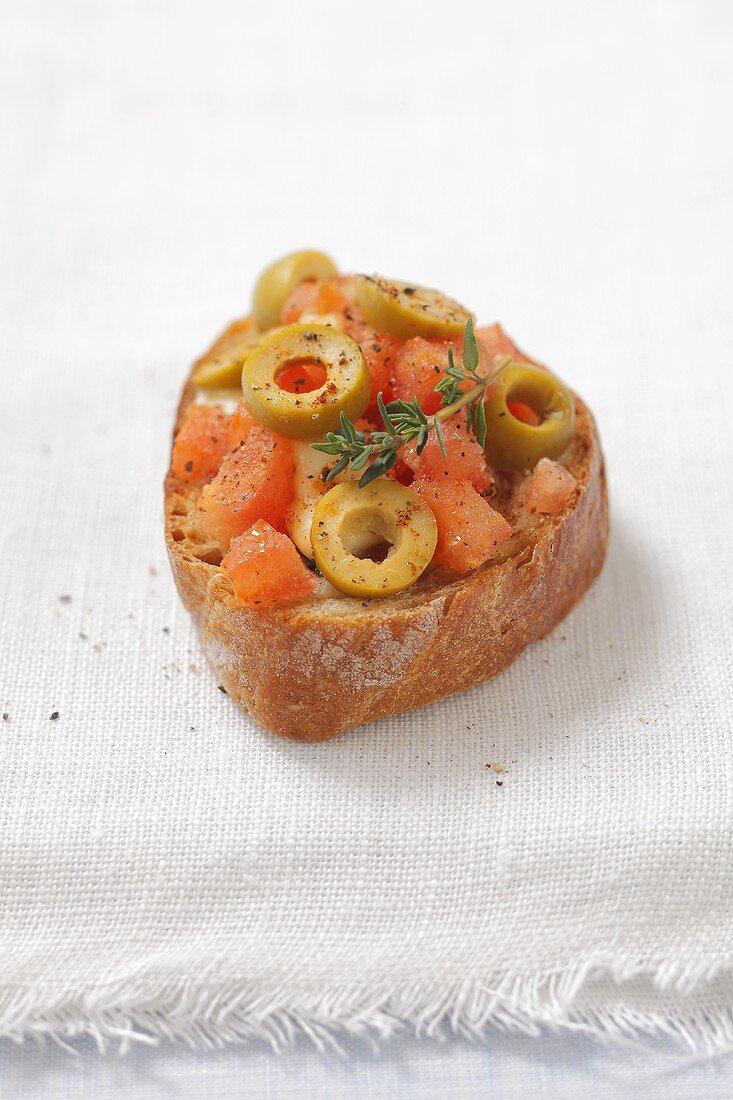 A toasted baguette slice topped with tomatoes, olives and mozzarella