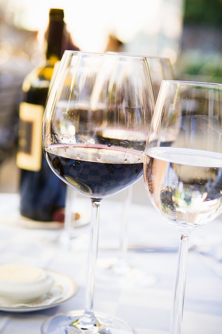 A glass of red wine and a water glass on a table laid outside