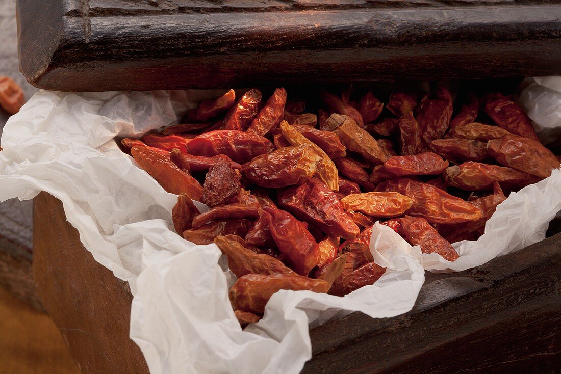 Dried chilli peppers on paper in a wooden crate