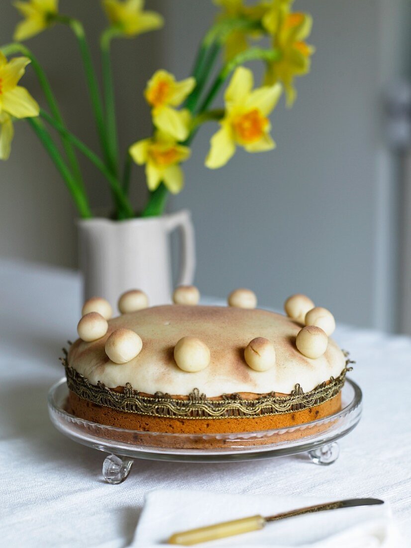 Kuchen auf Glasschale und Narzissen in Vase