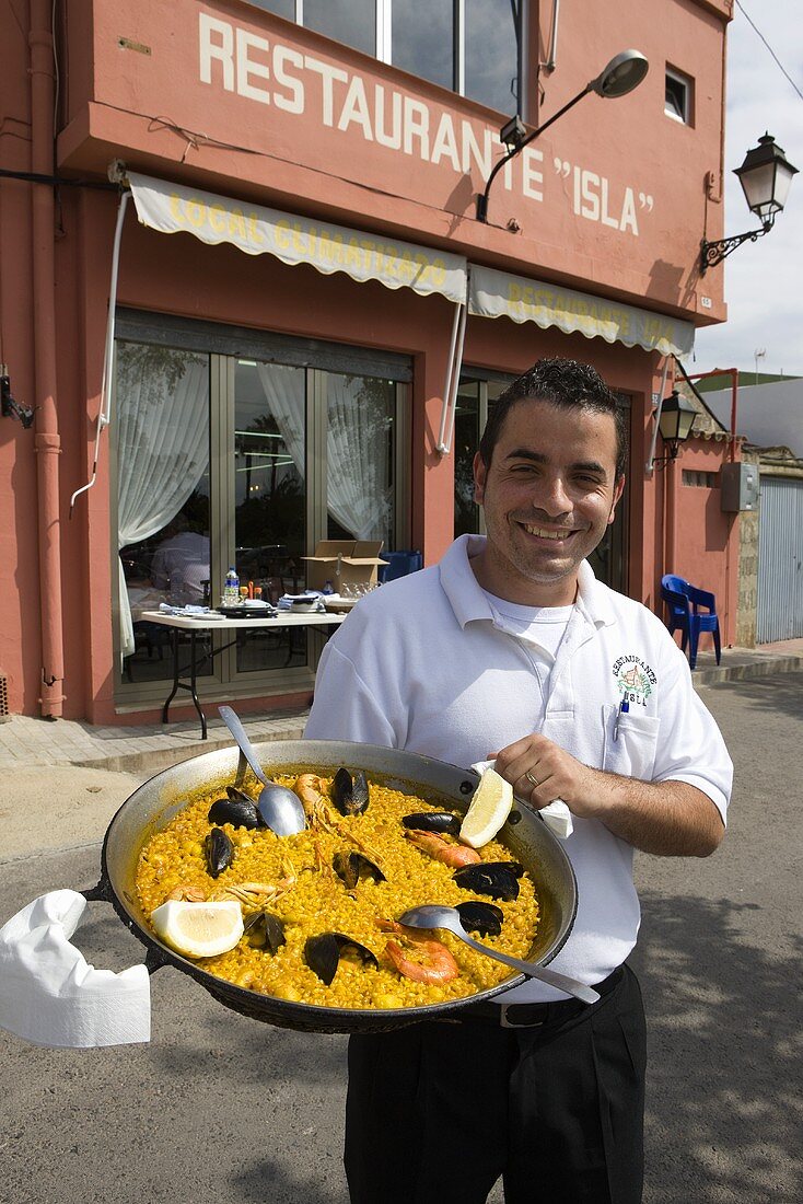 Kellner präsentiert Paella vom Restaurant Isla (El Palmer, Valencia, Spanien)