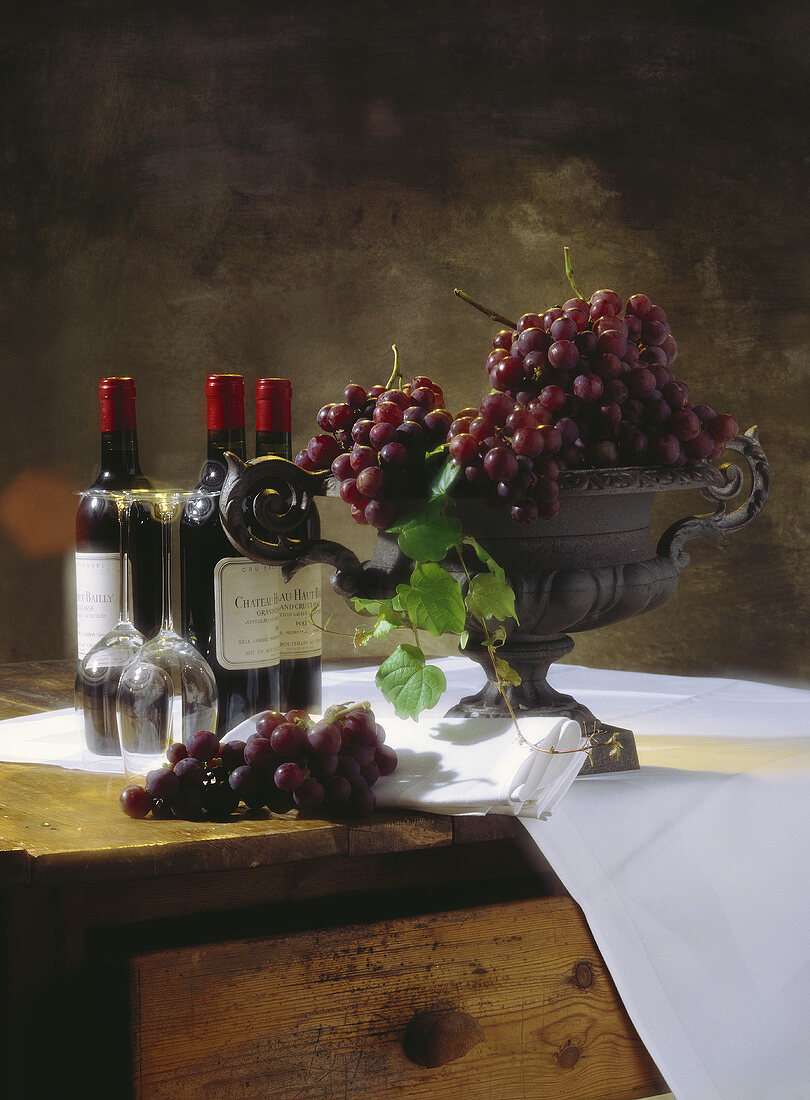 Rotweinstilleben mit Bordeaux-Flaschen und Weintrauben