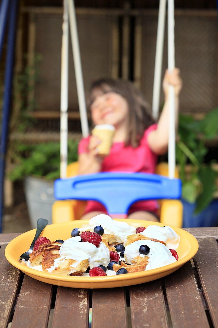 Pancakes with forest fruits on a wooden table and a girl in the background on a swing