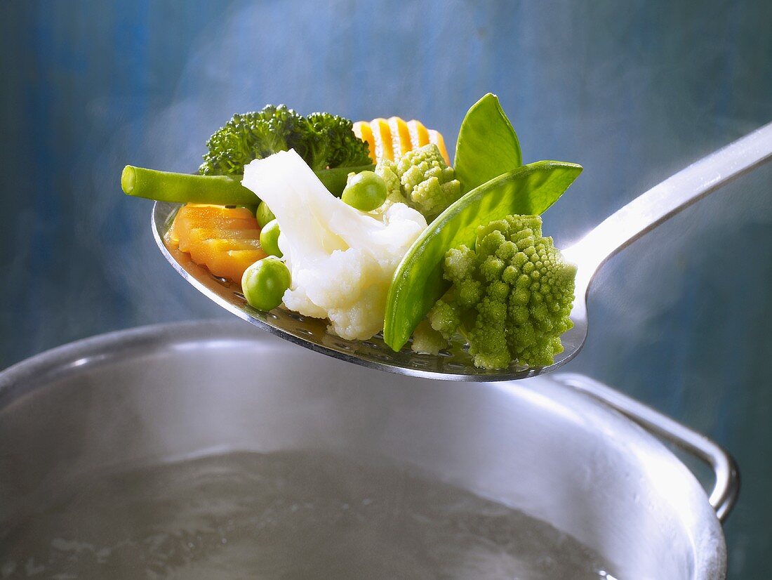 Mixed vegetables in a ladle over a saucepan