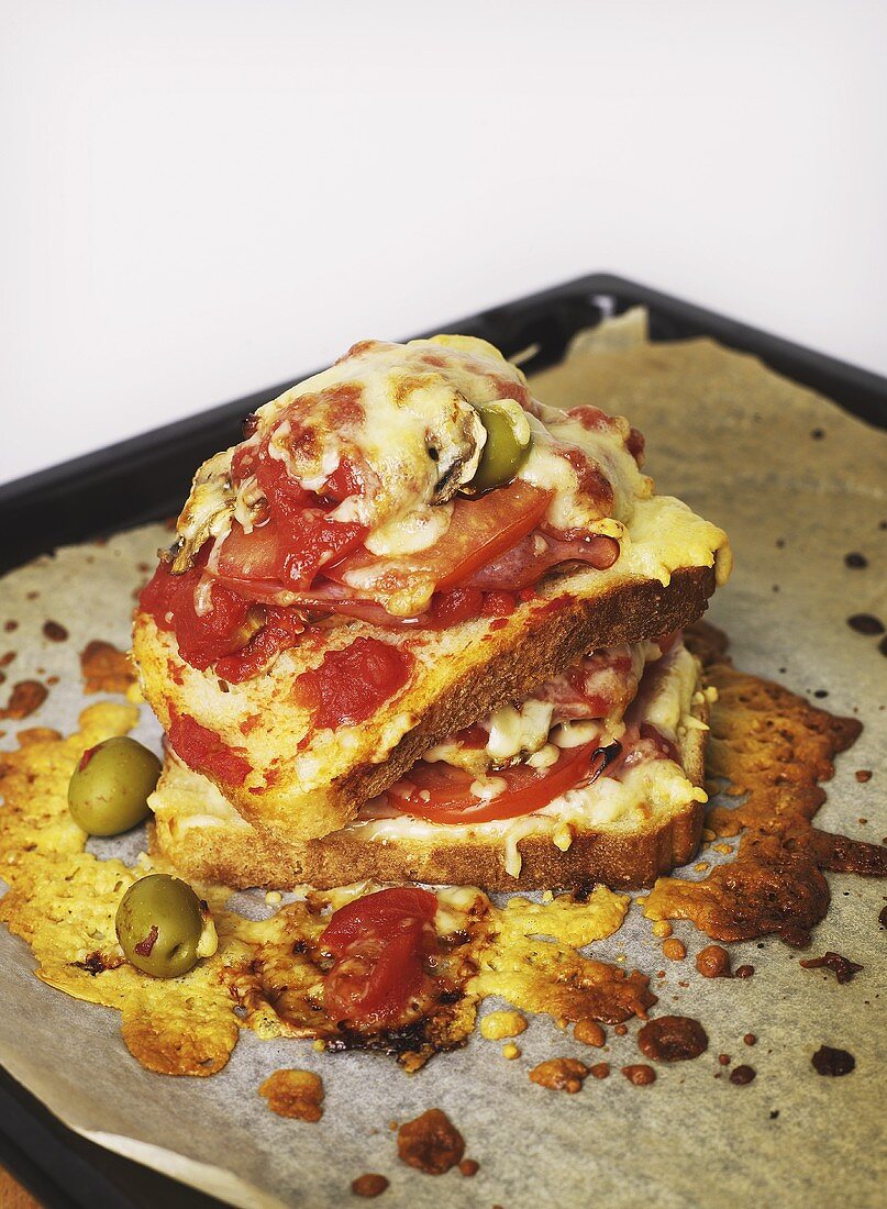 A toasted tomato, olive and cheese sandwich on a baking tray