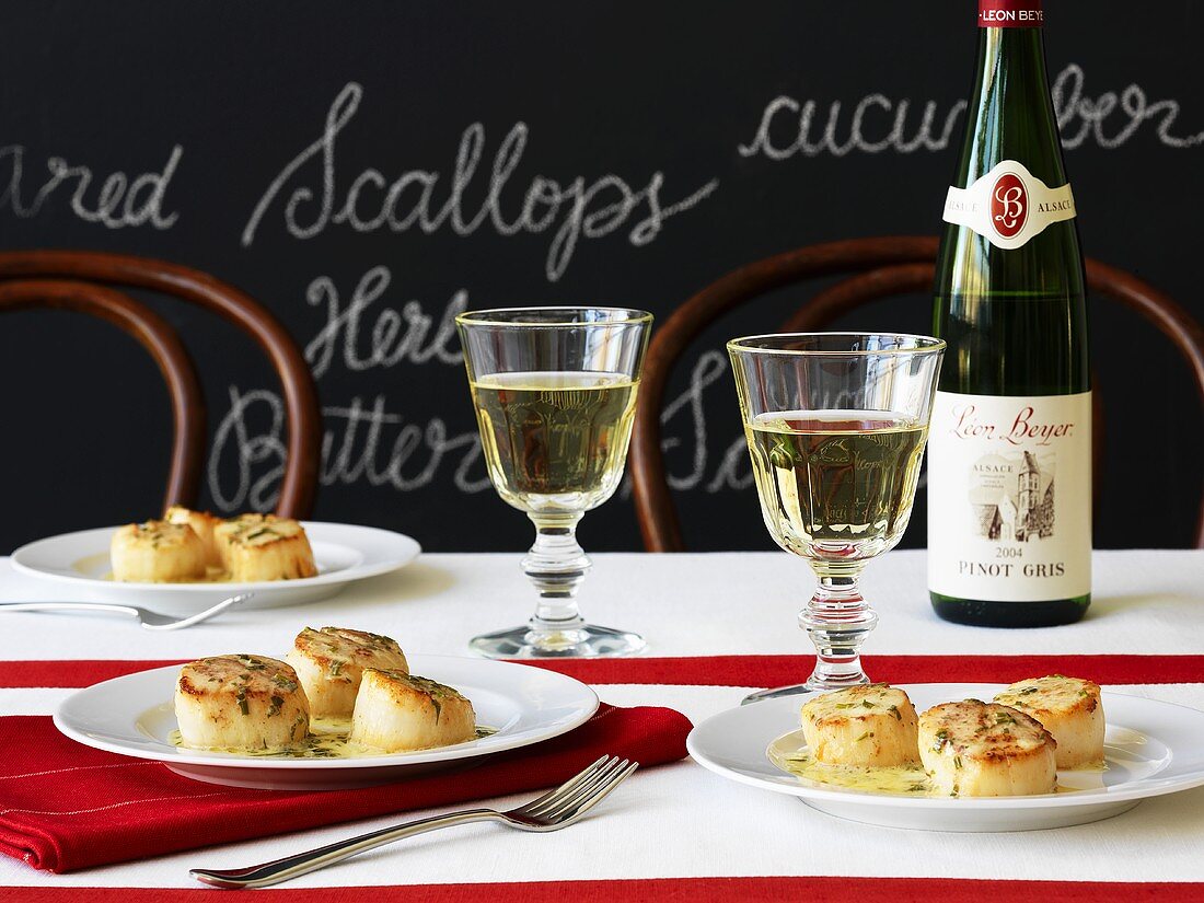 Scallops with herb butter and white wine in front of a blackboard with writing on