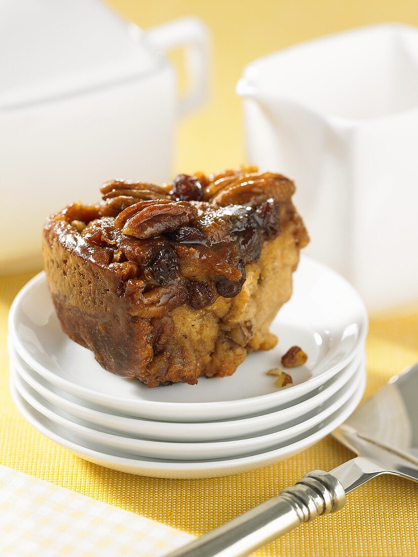 A cinnamon roll with pecan nuts and raisins on a stack of plates