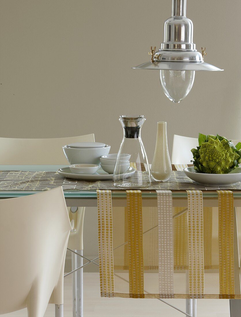 A dining table with a table runner, a carafe, a vase and Romanesco broccoli