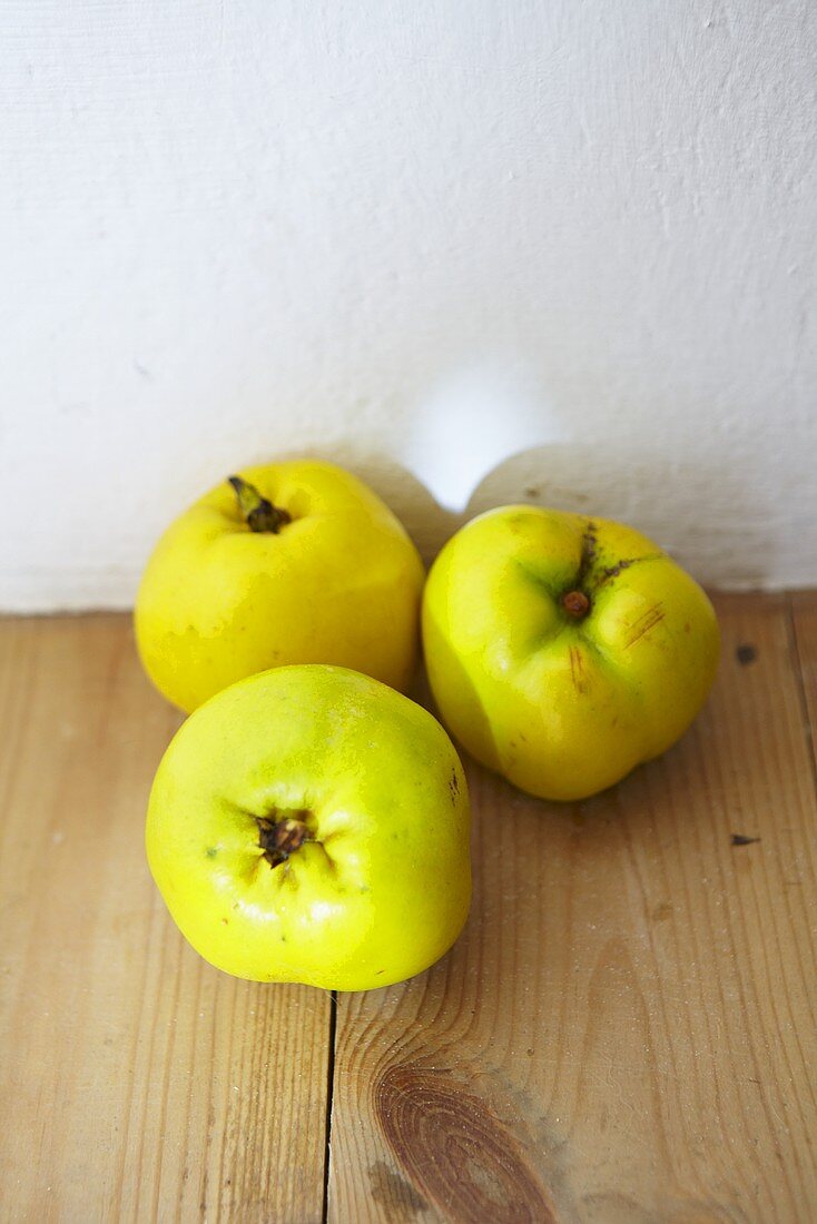 Three quinces on a wooden surface