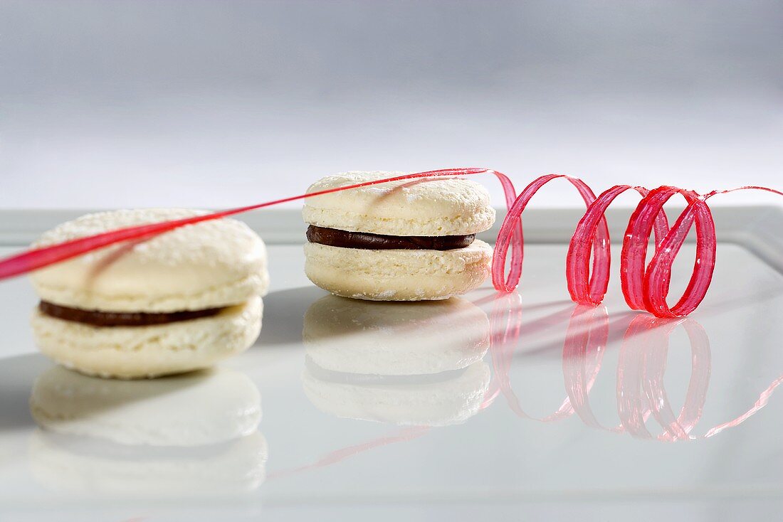Two white chocolate macaroons with a spiral of red icing sugar