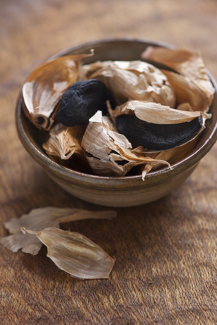 Black garlic, semi peeled, in a ceramic bowl