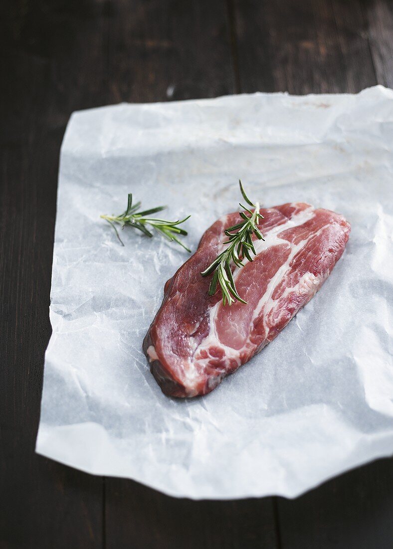 Raw beef steak and rosemary on a piece of paper