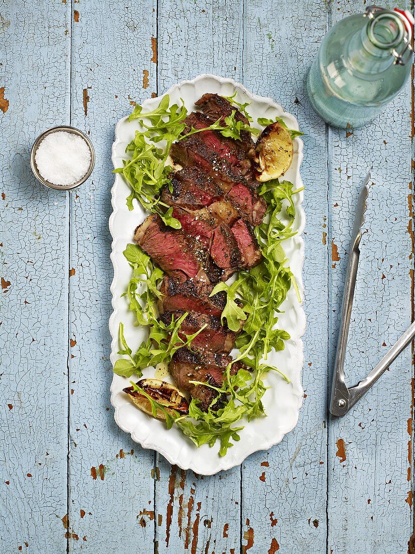 Sliced rib-eye steak with rocket on a serving dish