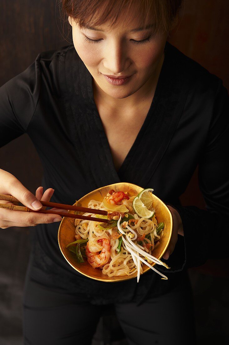 A woman eating pad thai (fried rice noodles, Thailand)