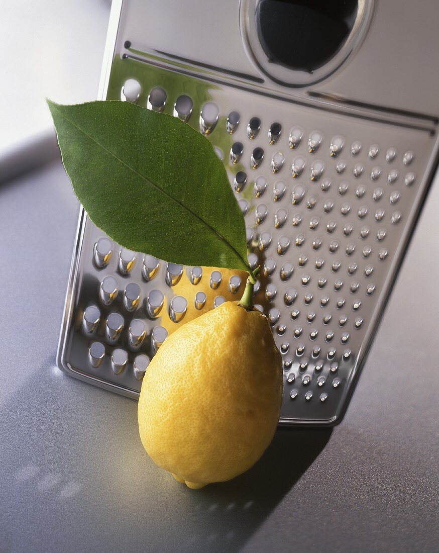 A lemon with a leaf in front of a grater