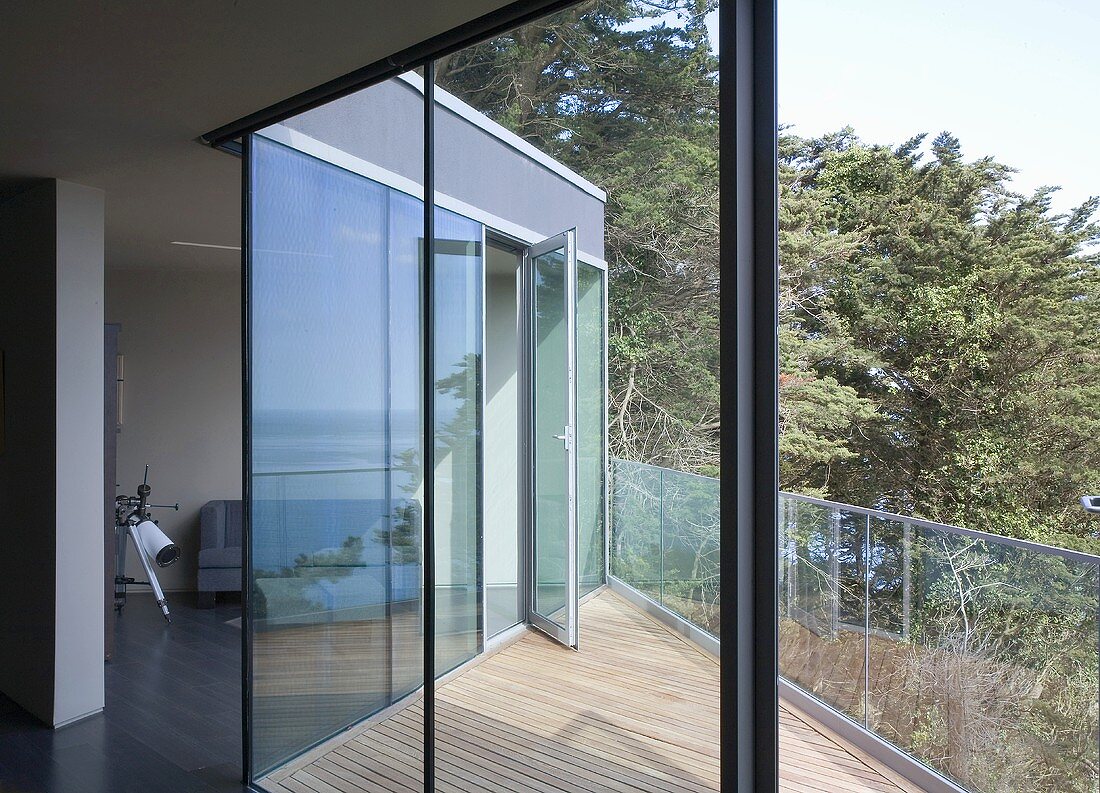 A modern house with a view through an open terrace door onto a terrace with wooden boards and a glass balustrade