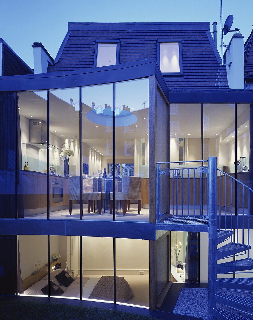 A modern house with external stairs against a glass facade with a view into the dining room and the bedroom