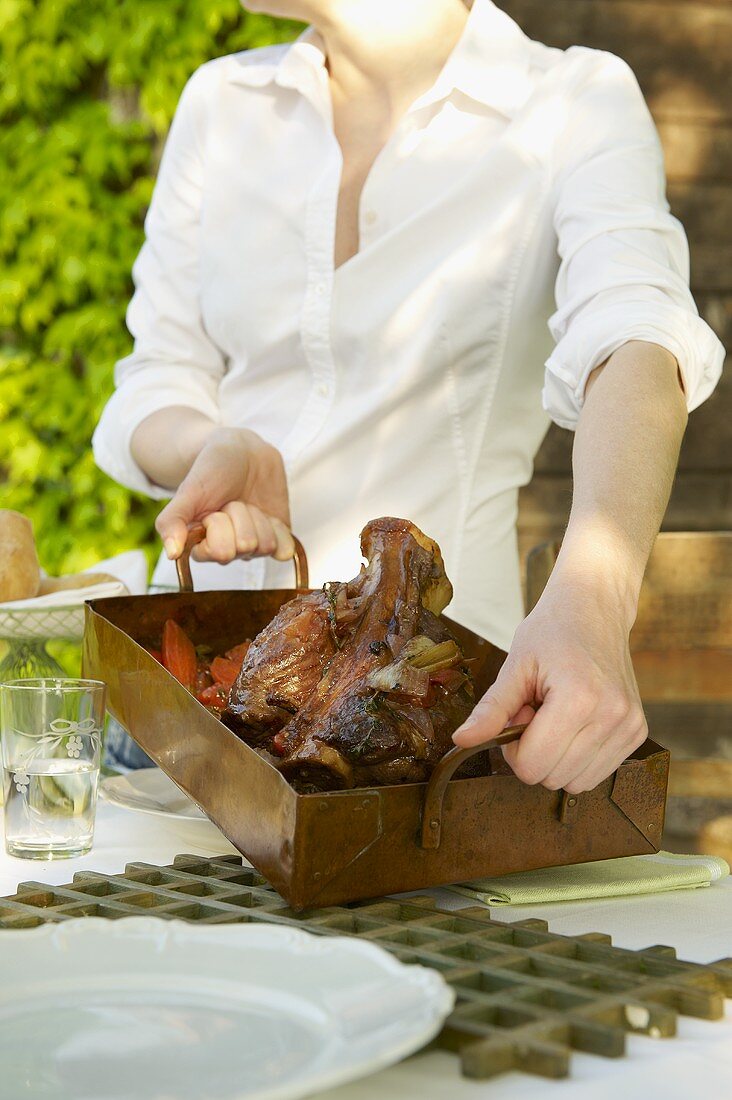 A woman holding a roast veal knuckle in a roasting tin