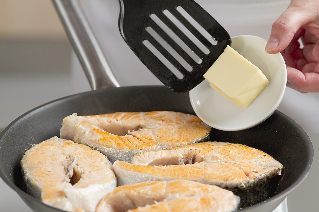 Butter being added to a pan of salmon steaks
