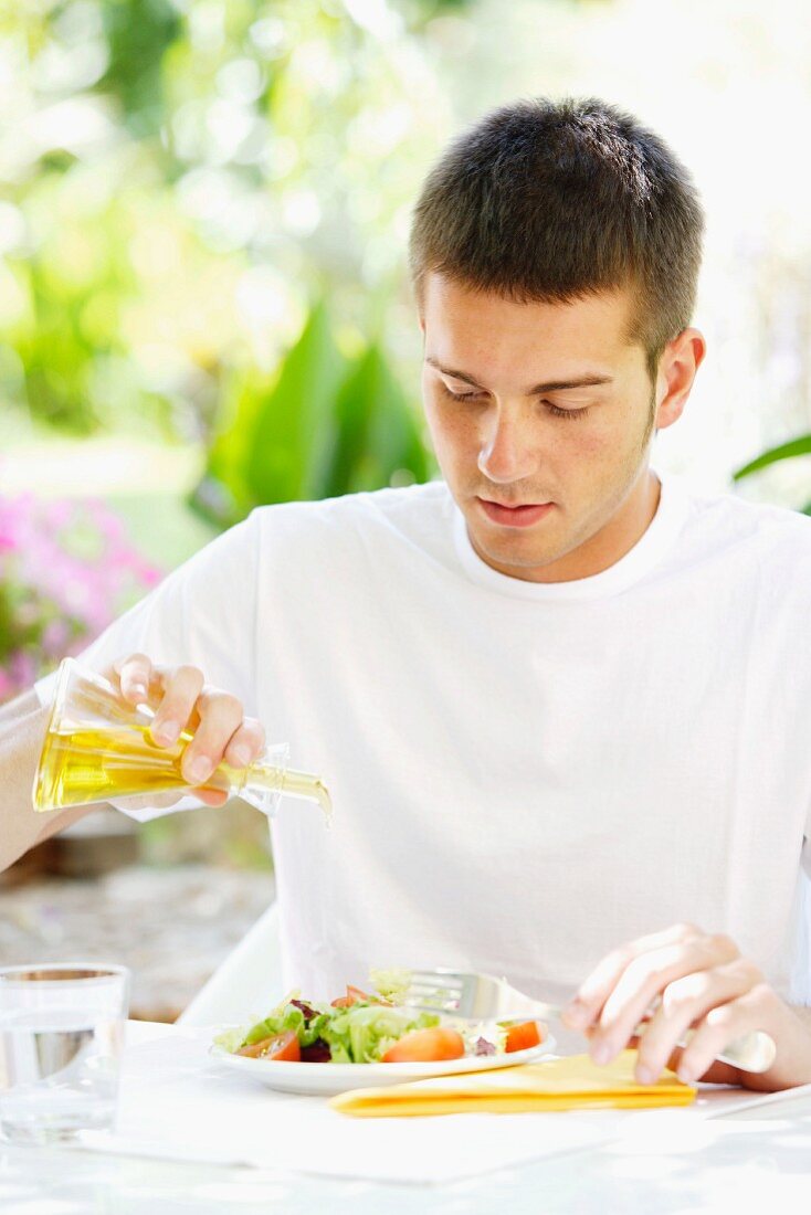 Young man drizzling oil on salad