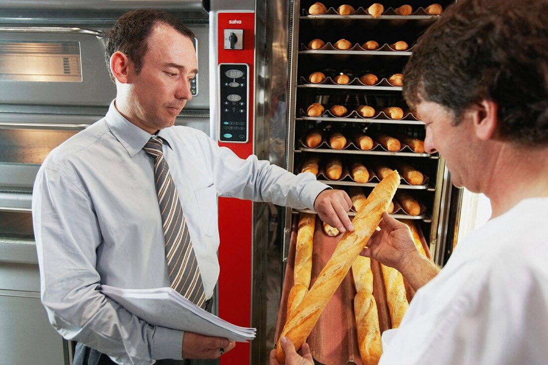 Technician and baker checking quality of bread, baking ovens