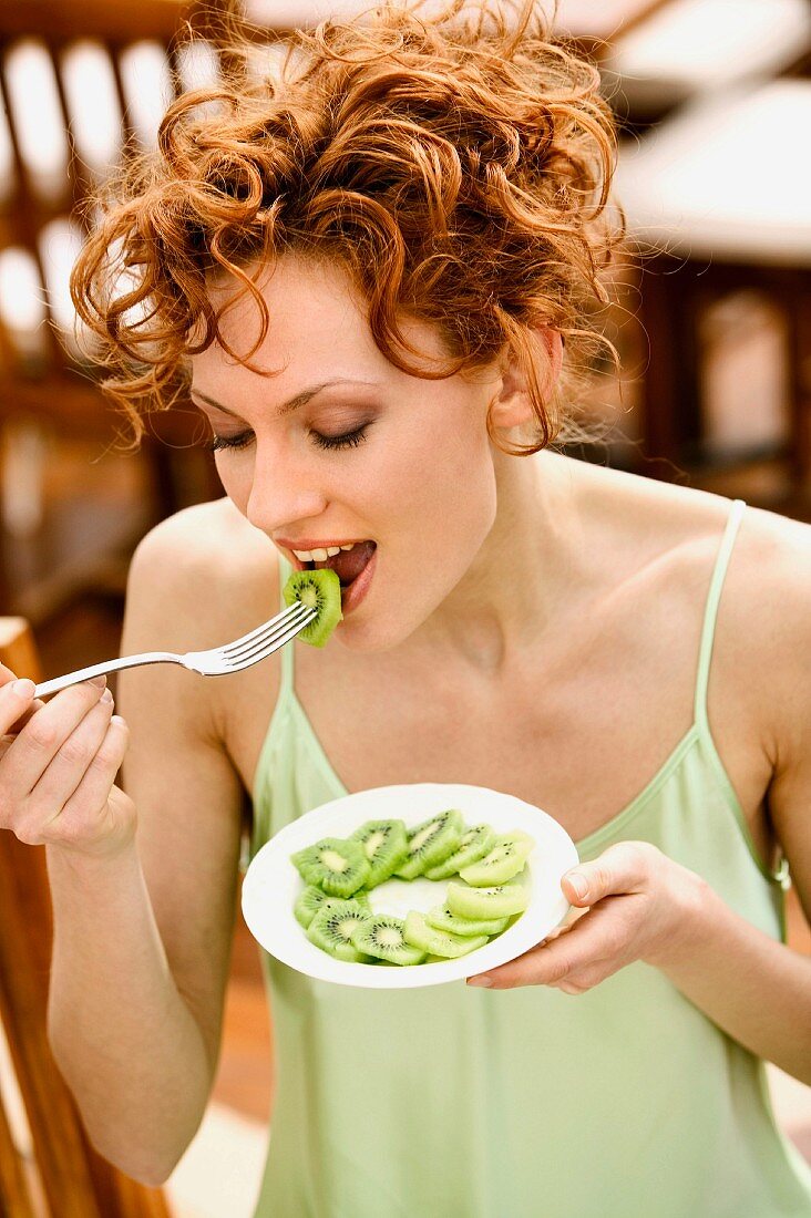 Young woman eating sliced kiwi fruit