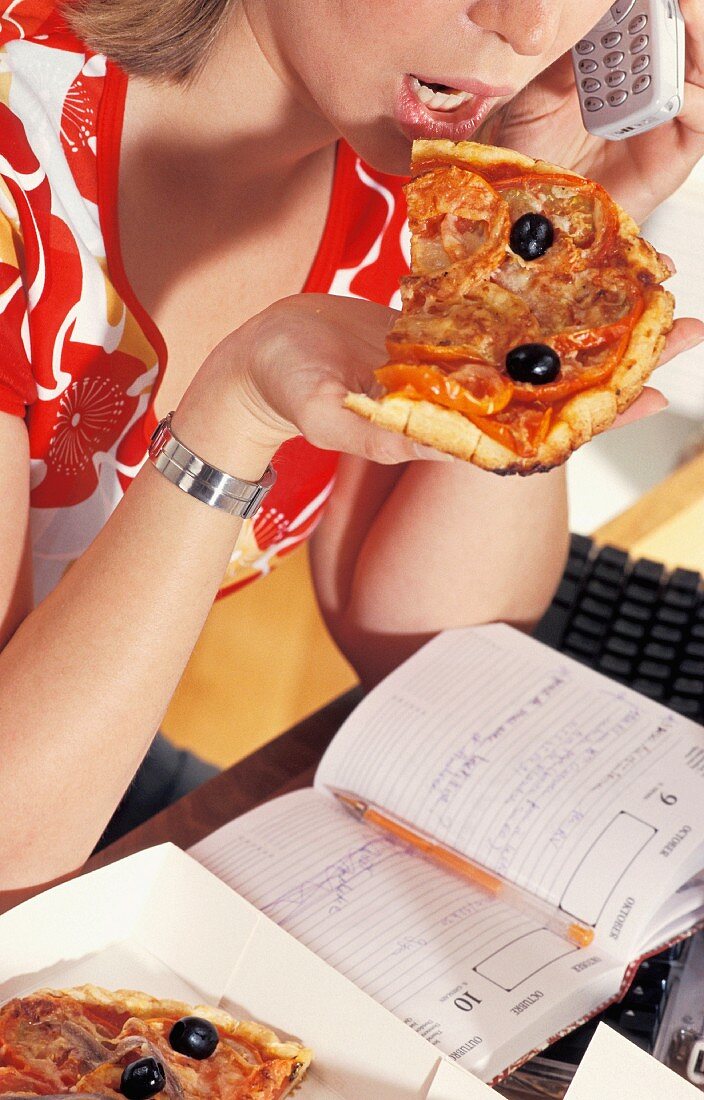 Junge Frau am Telefon isst ein Stück Pizza