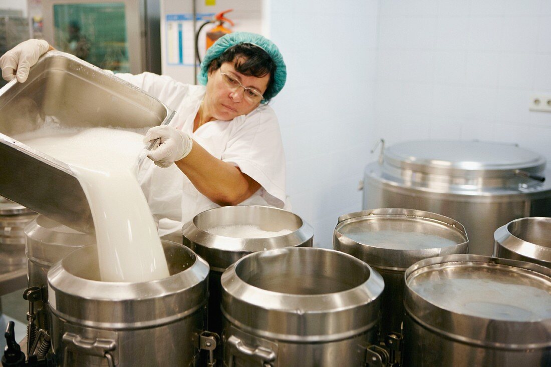 A woman pouring milk into a container in a commercial kitchen
