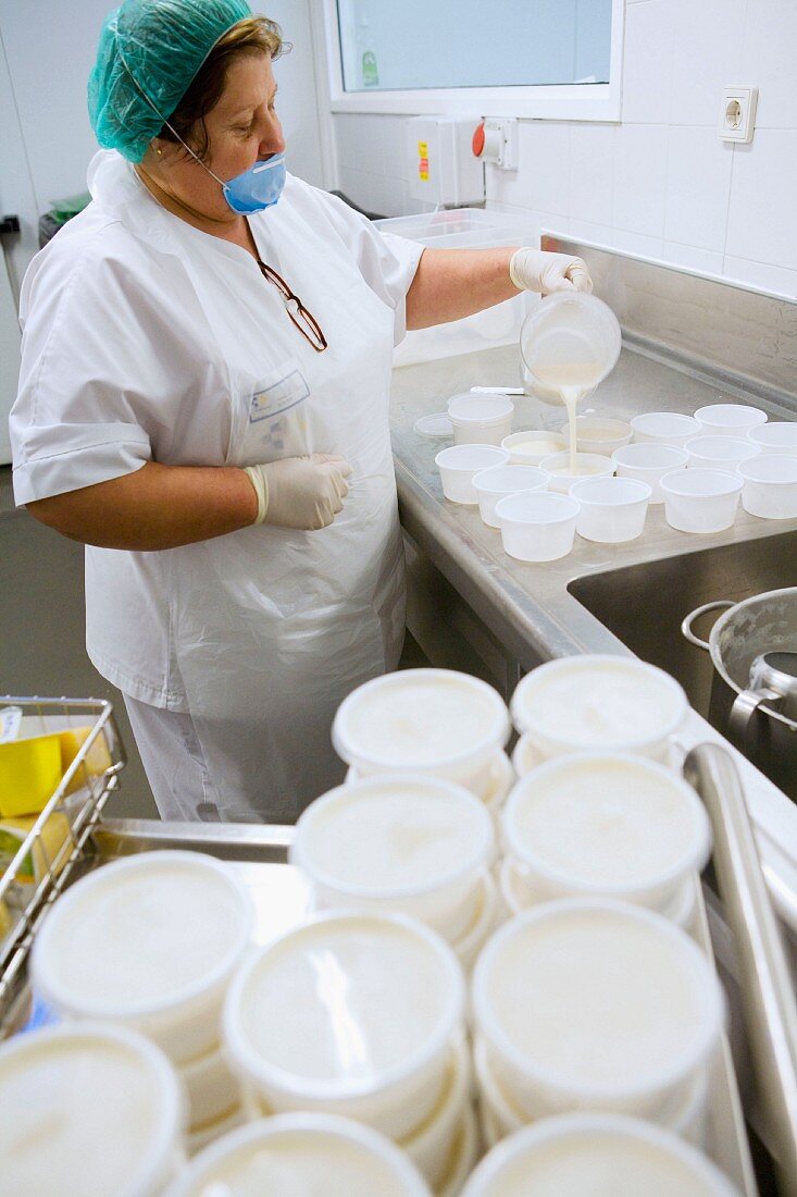 Woman putting dessert into plastic pots (canteen kitchen)
