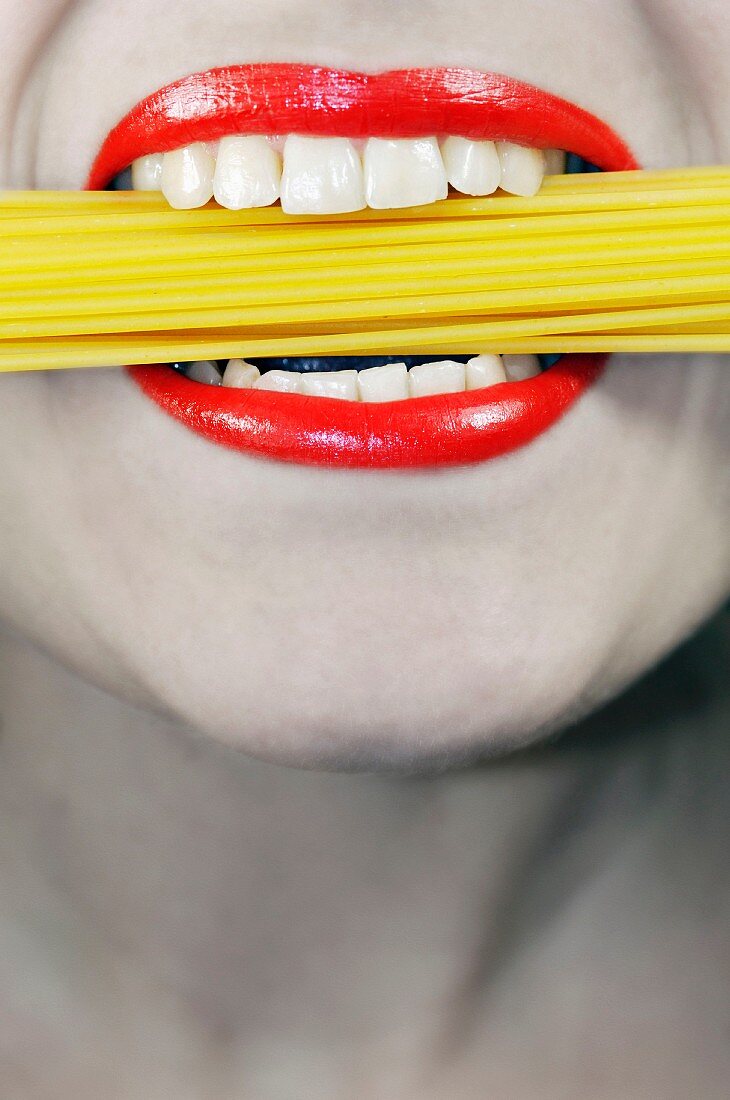 Frau mit ungekochten Spaghetti im Mund