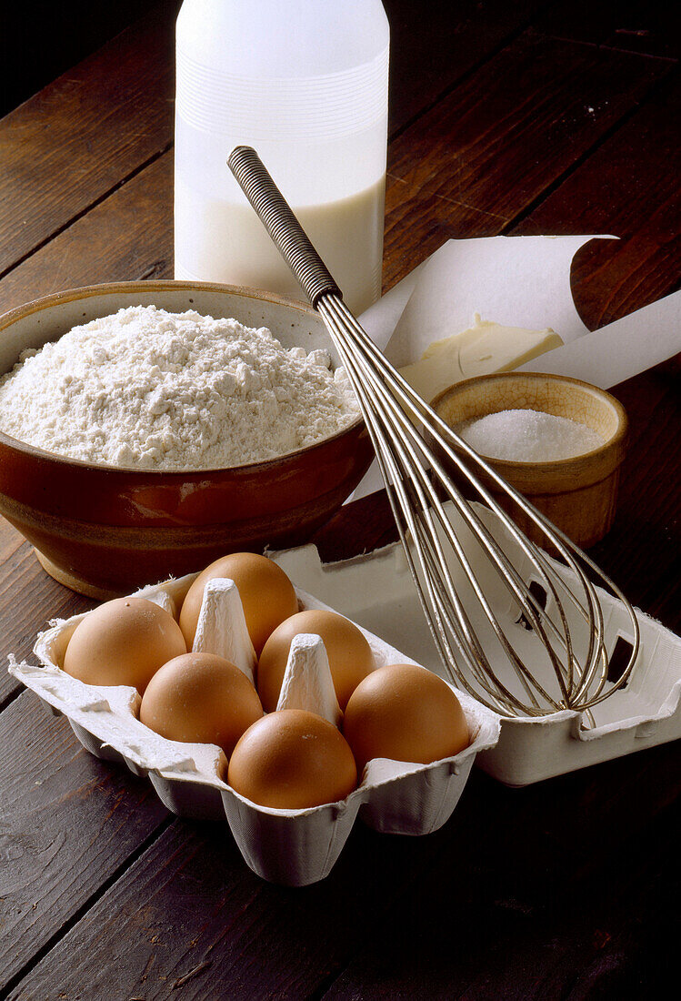 Zutaten für Crêpes auf Holzuntergrund: Eier, Milch, Mehl, Butter mit Schneebesen
