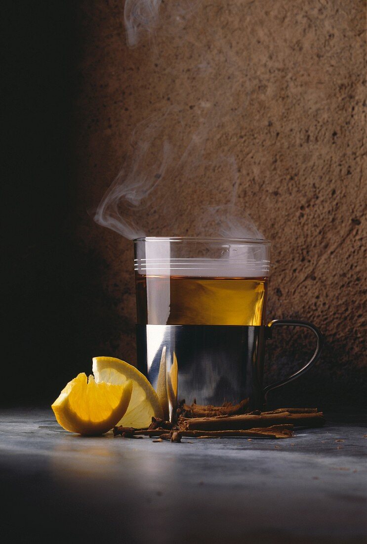 Dampfende Tasse Tee, Zitronenstücke und Zimtstangen