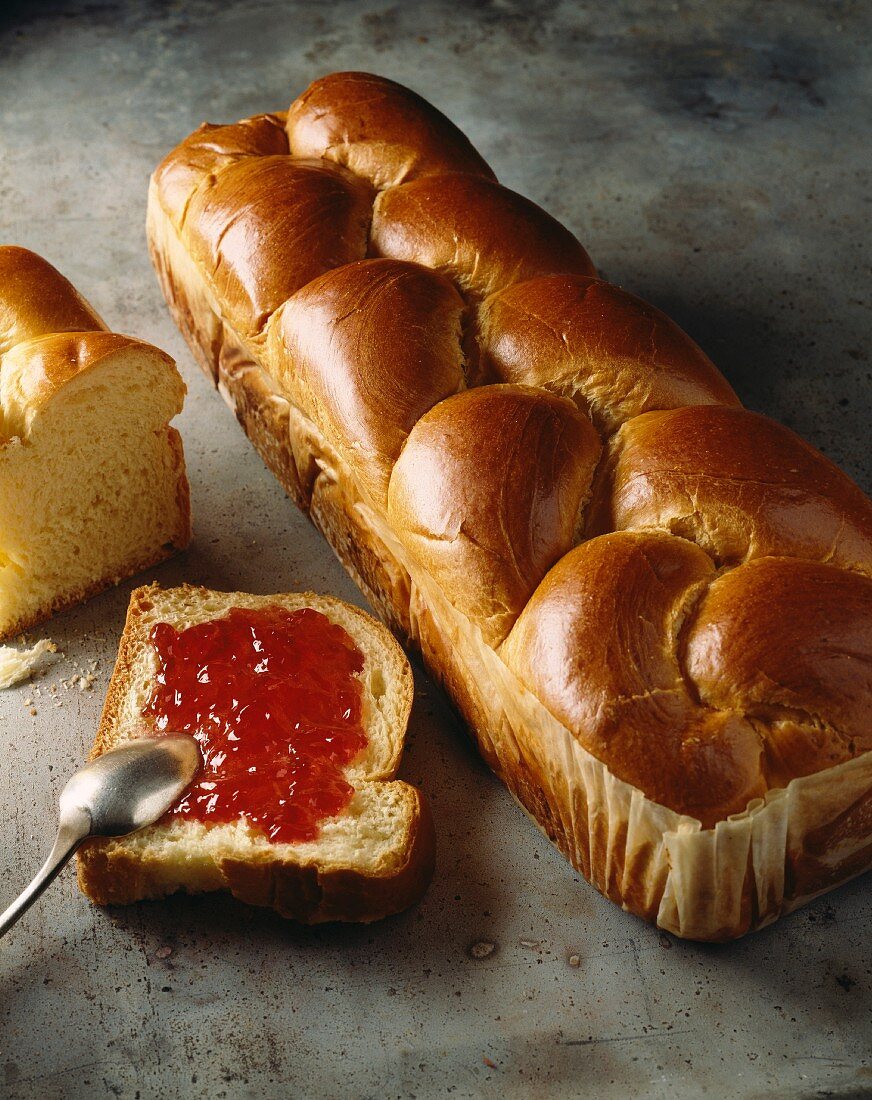 Ein Laib Brioche und Briocheescheibe mit Konfitüre