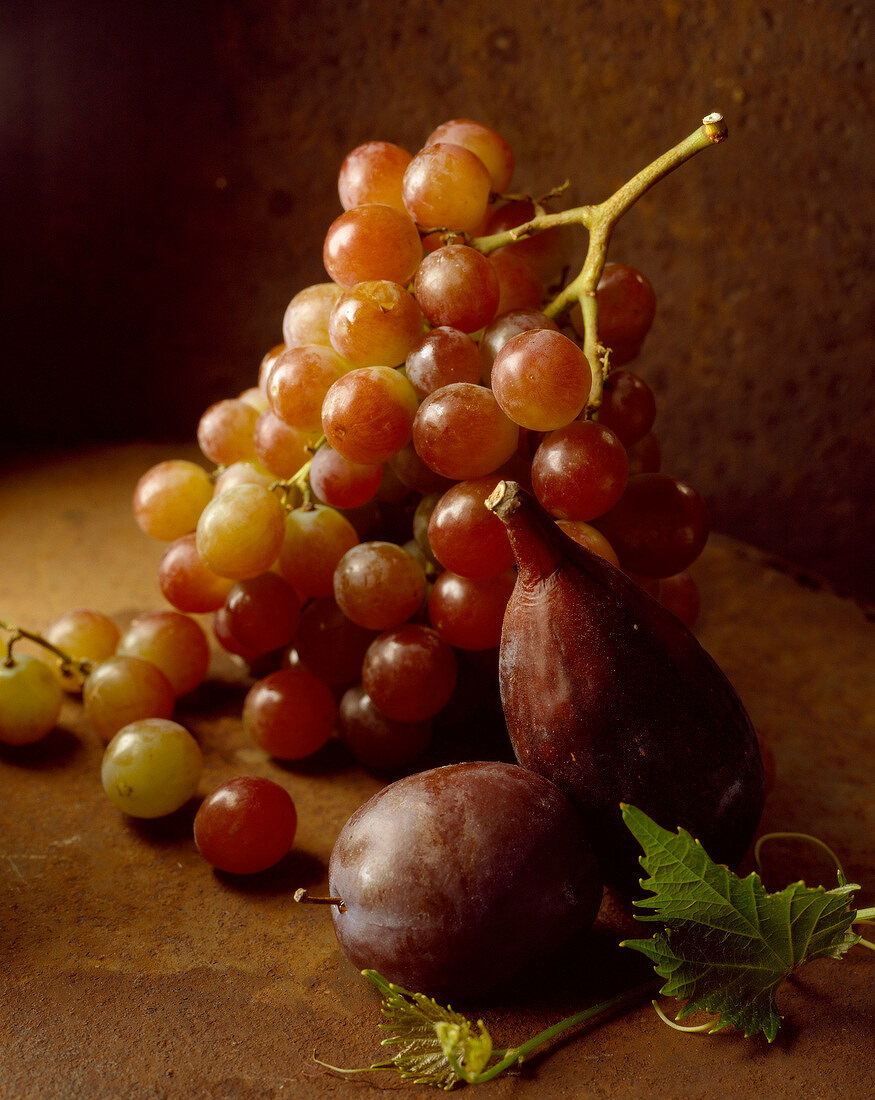 Frische Weintrauben, Feige und Pflaume auf braunem Untergrund