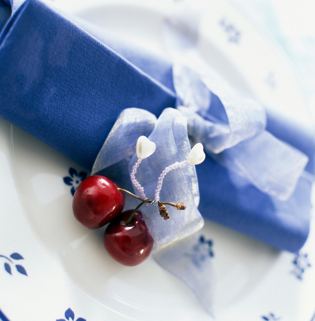 Blaue Stoffserviette mit Schleife und Kirschen als Tellerdekoration