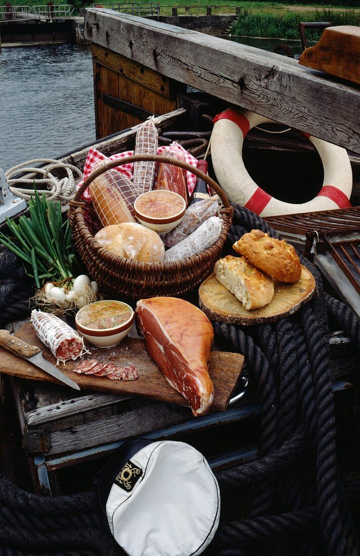 Stillleben aus verschiedenen Wurstwaren im Korb und auf Schneidebrett mit Brot auf einem Fischerboot