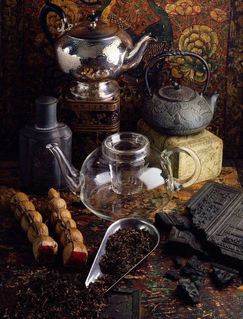 Tee-Stillleben mit verschiedenen Teekannen, Teeblättern und Ziegeltee