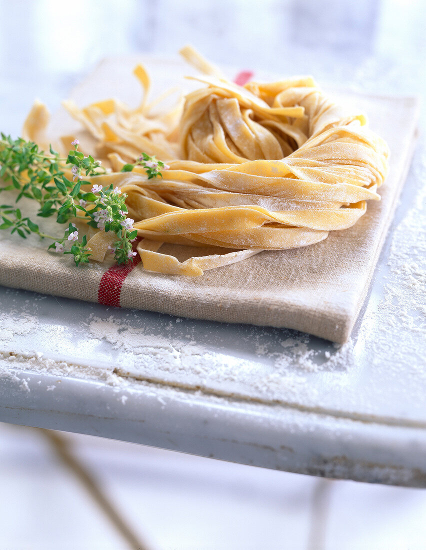 Frische Eier-Tagliatelle mit Thymian und Geschirrtuch auf bemehlter Arbeitsfläche