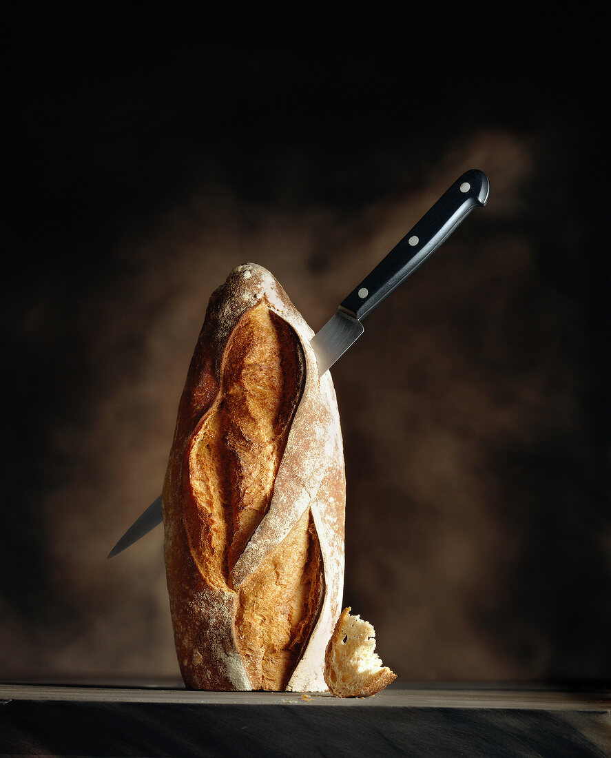 Ein spitzes Messer steckt in einem halben, aufrecht stehenden Baguette