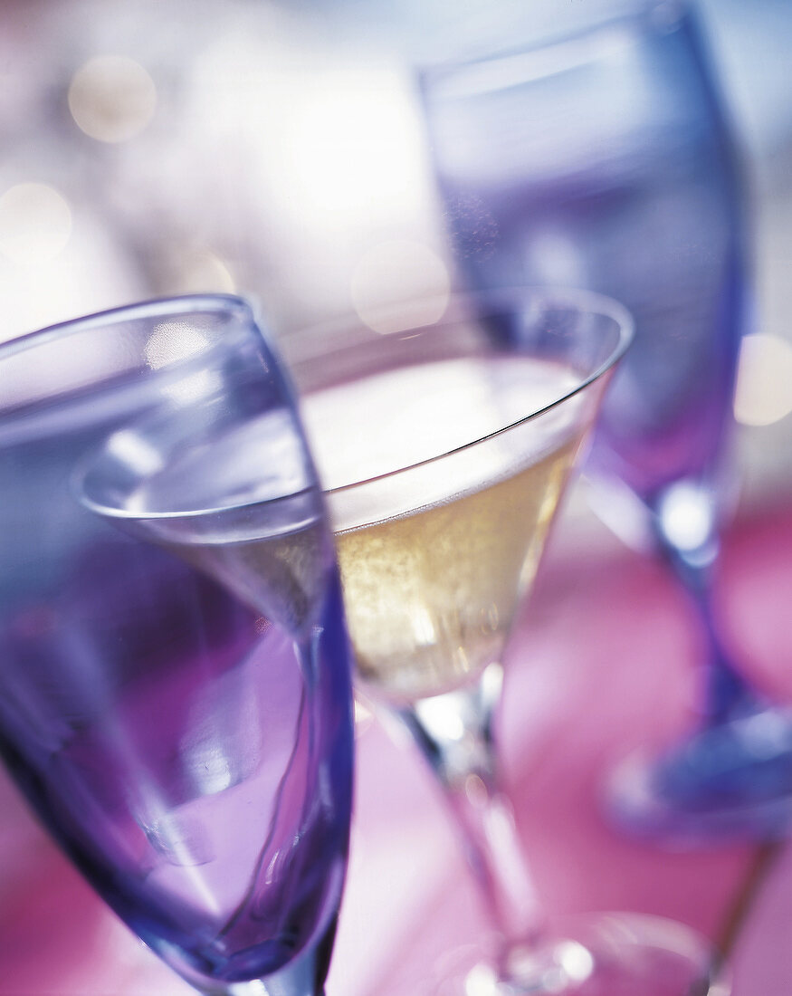Ein Glas Champagner zwischen zwei blauen, leeren Gläsern