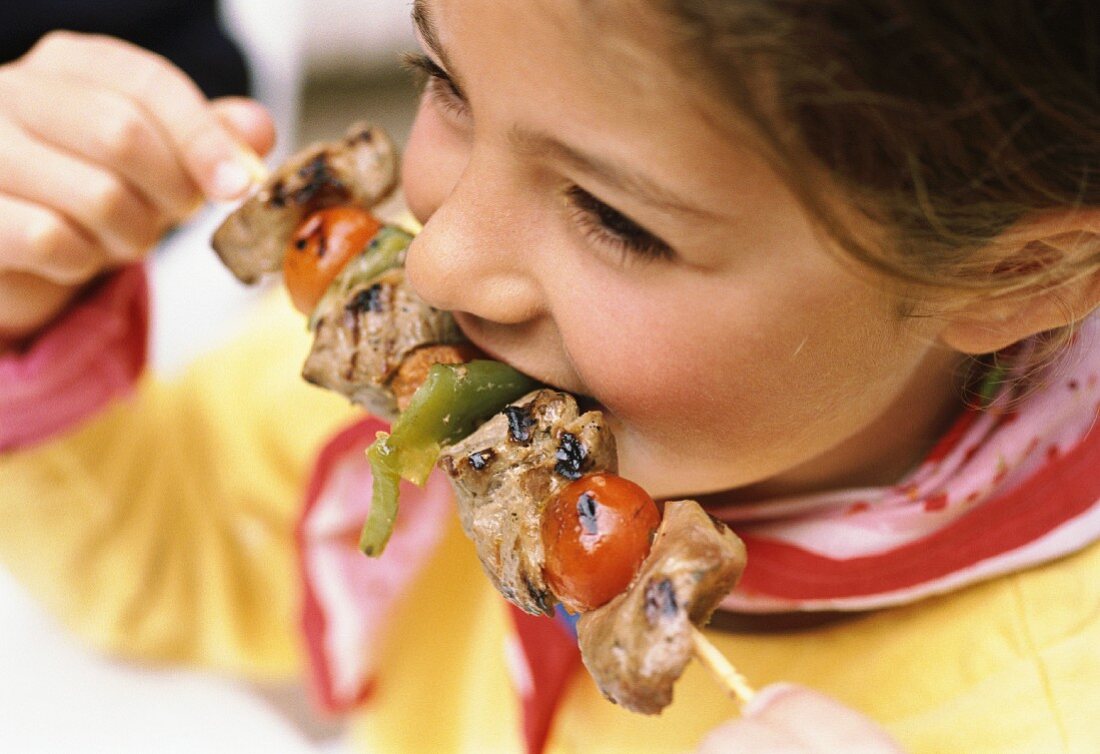 Child eating meat and pepper shish kebab