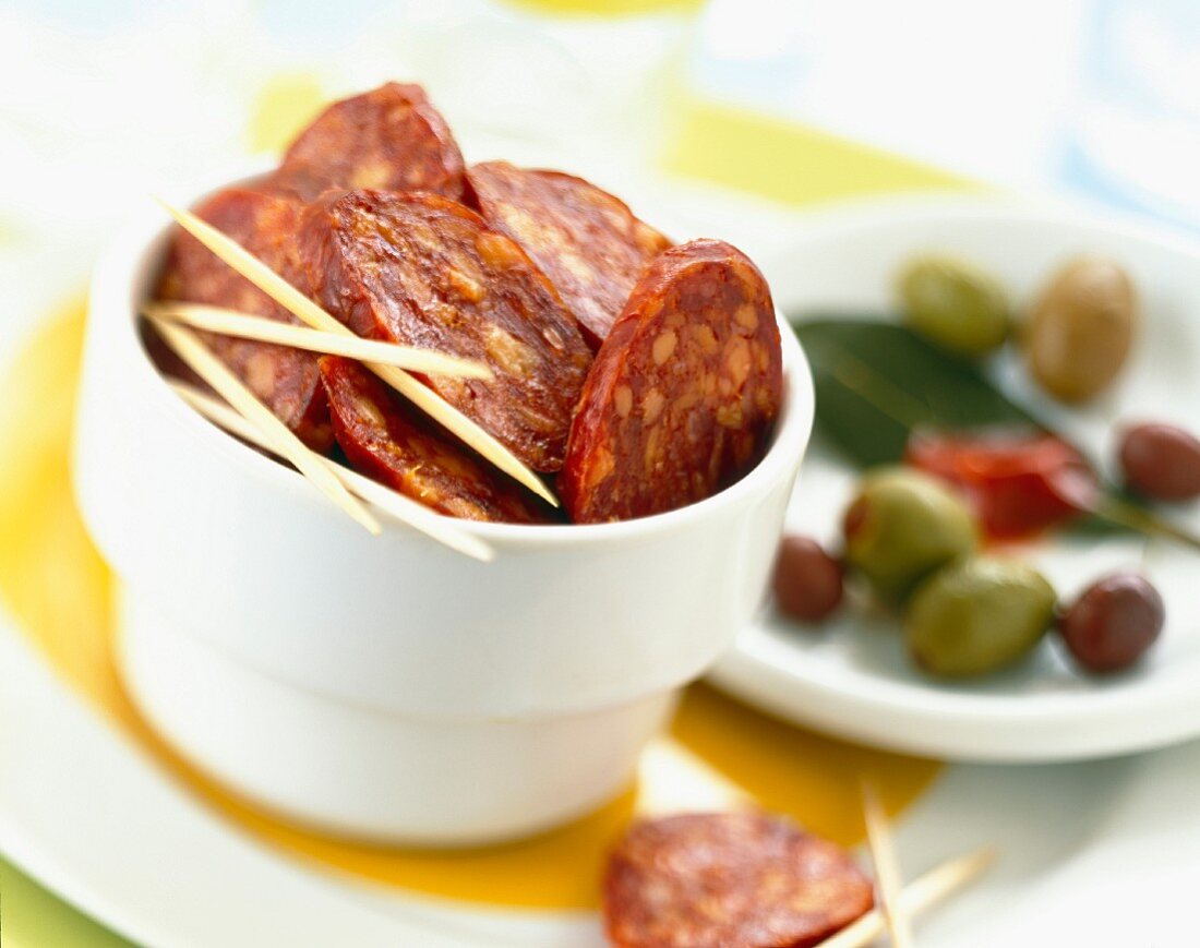 Chorizo-Scheiben mit Holzspiesschen und Oliven zum Aperitif