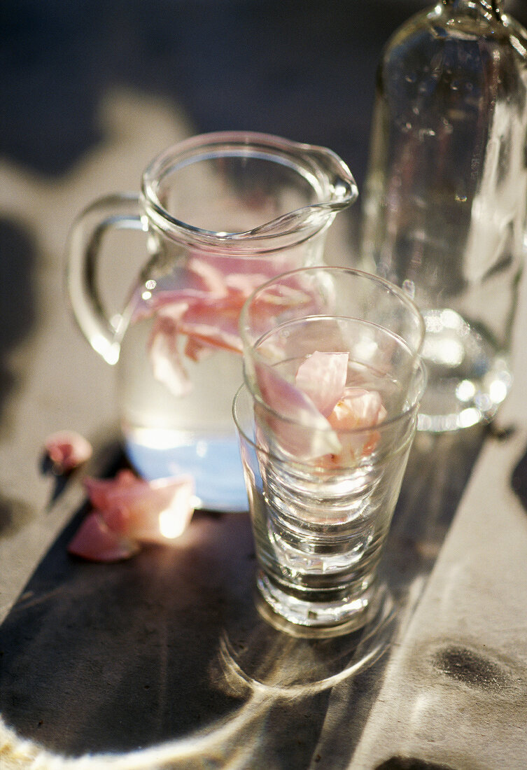 Karaffe mit Wasser und Rosenblütenblättern, dazu Gläser