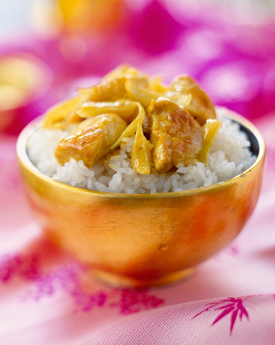Reis und sautiertes Geflügel mit Curry in goldenem Schälchen