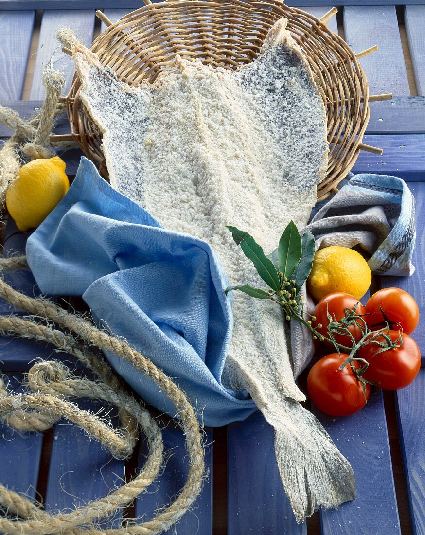 Stockfisch mit Tomaten, Lorbeer, Zitronen und Hanfstrick auf blauem Holzuntergrund