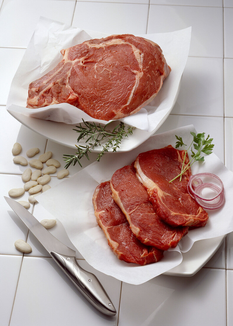 Rohe Lendensteaks und Koteletts vom Rind mit Kräutern und Zwiebelringen auf Papier