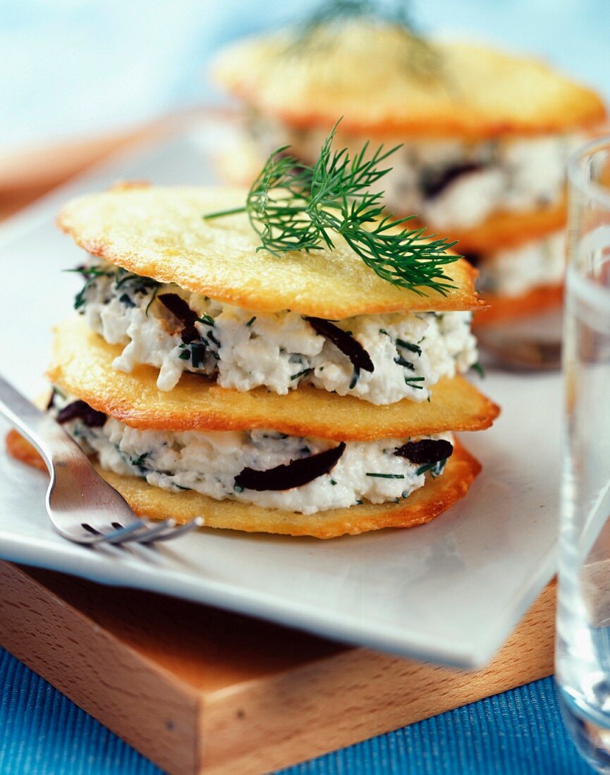 Layered thin cheese biscuits and fromage frais with olives